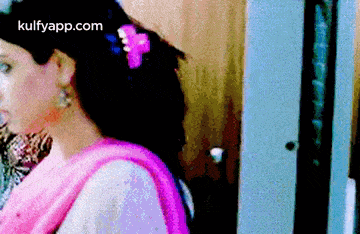 a woman in a pink dress with a flower in her hair is standing next to a door .