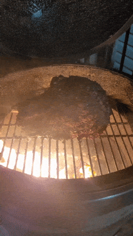 a large piece of meat is cooking on a grill with flames behind it