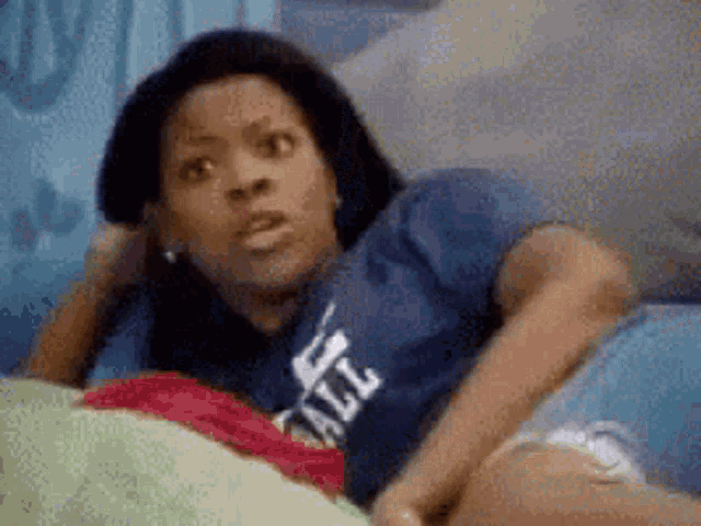 a woman in a blue shirt with the word all on it is laying on a bed .