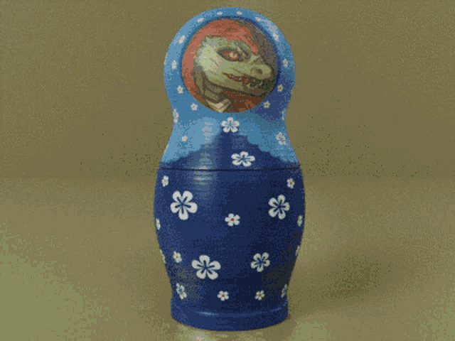 a blue green and orange nesting doll with a picture of a dinosaur on it