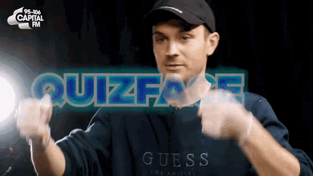 a man in a guess sweatshirt is dancing in front of a capital fm logo