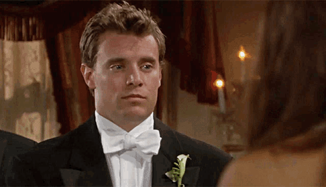 a man in a tuxedo with a bow tie looks at a woman