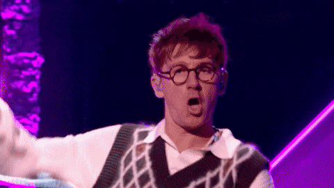 a man wearing glasses and a sweater is making a funny face on a stage .