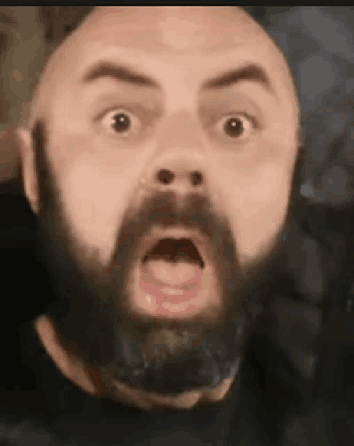 a bald man with a beard is making a surprised face with his mouth open .