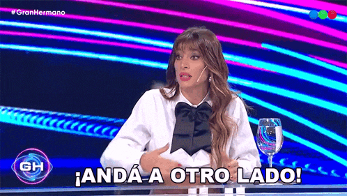 a woman is sitting at a table with a glass of water and says andá a otro lado .