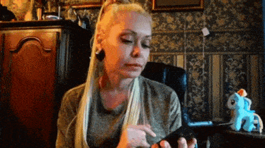 a woman with long blonde hair is sitting in a chair looking at her phone .