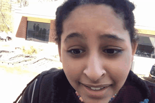 a woman with a nose ring is smiling in front of a brick house