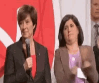two women are standing next to each other in front of a red and white flag .