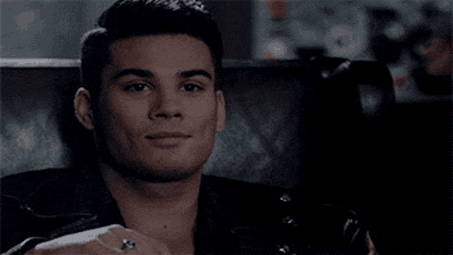 a man in a leather jacket is sitting in a chair with his hand on his chest .