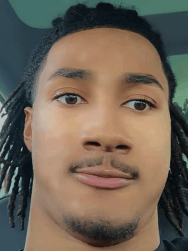 a young man with dreadlocks and a beard looks at the camera