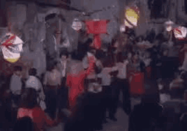 a blurry picture of a crowd of people dancing in a room with lanterns hanging from the ceiling .