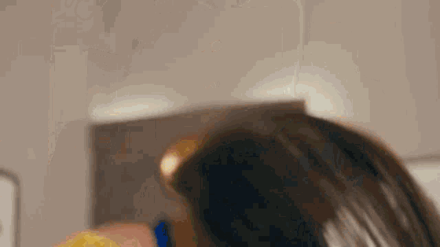 a woman in a yellow shirt and blue lanyard is holding her hair in a ponytail .