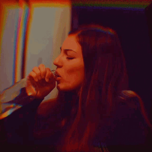a woman is drinking from a glass with a rainbow colored background