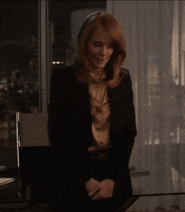a woman with red hair is standing in front of a window wearing a black jacket .