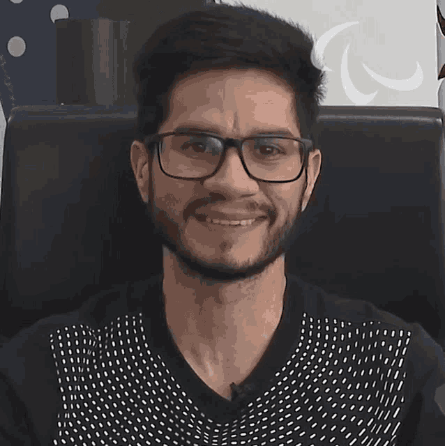 a man wearing glasses and a polka dot shirt smiles