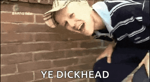 a boy leaning against a brick wall with the words ye dickhead written below him