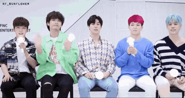 a group of young men are sitting in a row holding lightsticks with the name nf sunflower in the corner