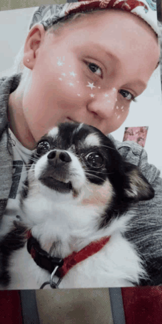 a girl with stars painted on her face holds a small black and white dog