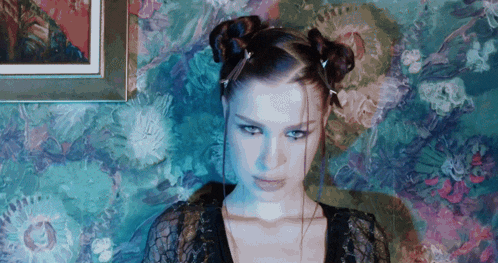 a woman with two buns in her hair is standing in front of a floral wallpaper