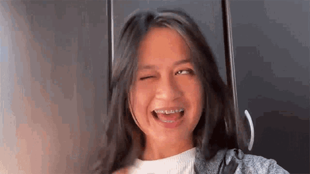 a girl with braces on her teeth is winking at the camera .
