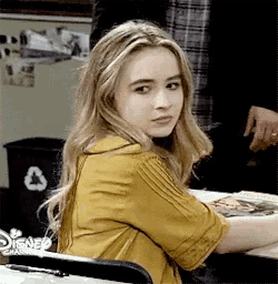 a woman in a yellow shirt is sitting at a table with a disney logo on it .
