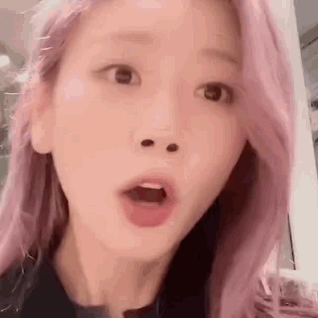 a close up of a woman 's face with pink hair making a funny face .