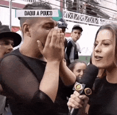 a man covering his mouth while a woman holds a microphone with the words daqui a pouco on the bottom
