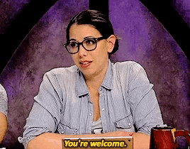 a woman wearing glasses sits at a table with a sign that says you 're welcome