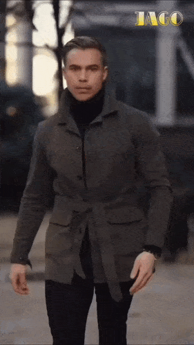a man wearing a jacket and a turtleneck is walking down a street .