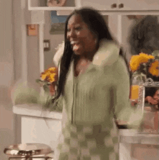 a woman in a green and white checkered dress is standing in a kitchen and smiling .