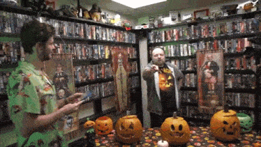 two men are standing in front of a table with pumpkins on it in a room filled with books .