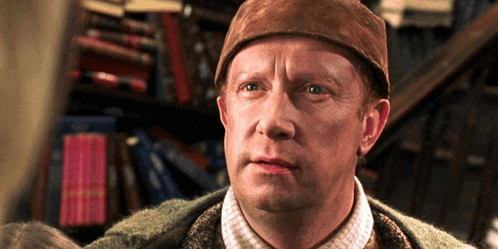 a man wearing a brown hat and sweater stands in front of bookshelves