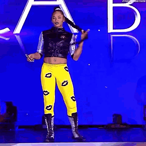 a woman in a crop top and yellow pants is walking on a stage with a mustache .