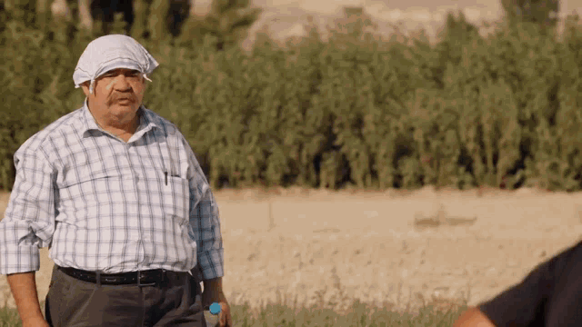 a man in a plaid shirt is standing in a field with trees in the background