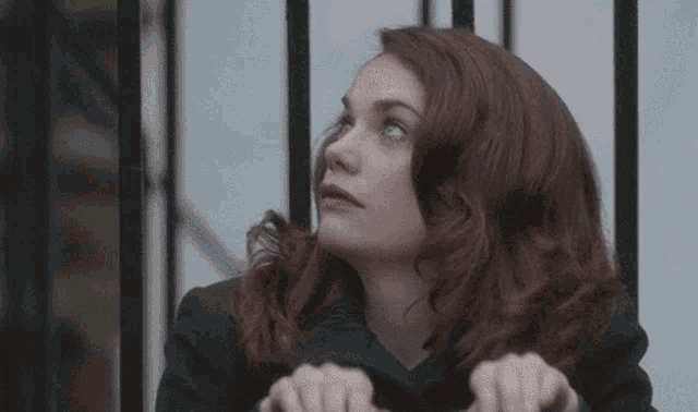 a woman with red hair is standing in front of a fence and looking up .