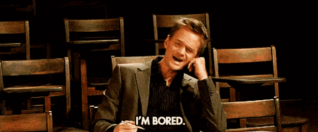 a man in a suit says i 'm bored in front of a row of wooden chairs