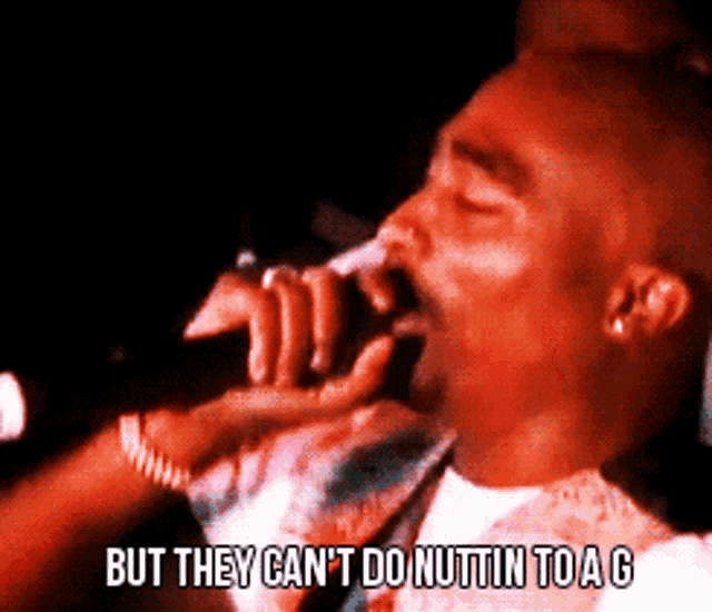 a man is singing into a microphone with the words but they can 't do nuttin to a g below him