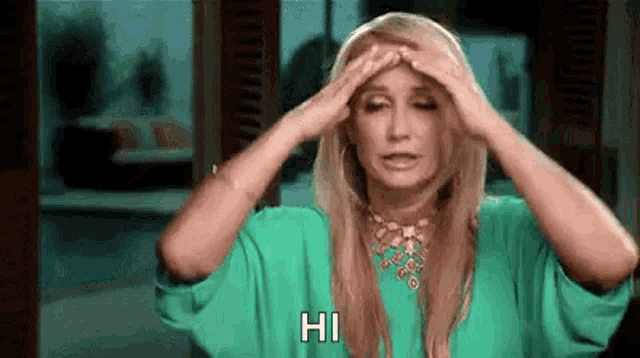 a woman in a green shirt is holding her head and says hi .