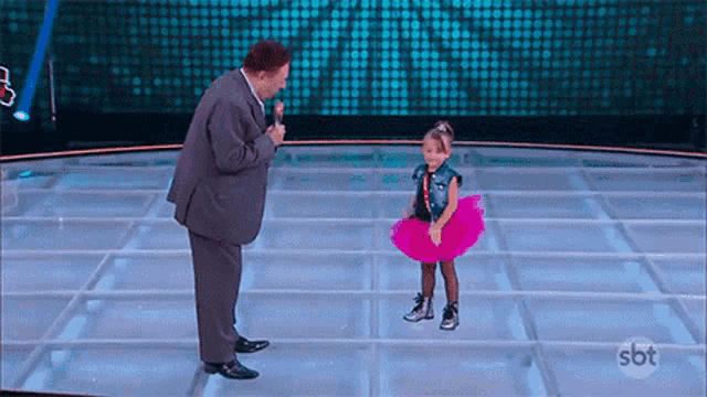 a little girl in a pink tutu is dancing next to a man in a suit on a stage .