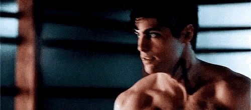 a shirtless man is standing in front of a punching bag in a boxing ring .