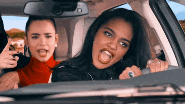 two women singing in a car with the letter d on the rearview mirror
