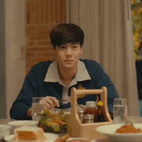 a young man is sitting at a table eating a salad .