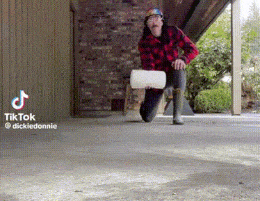a man in a plaid shirt is kneeling on the ground holding a white barrel .