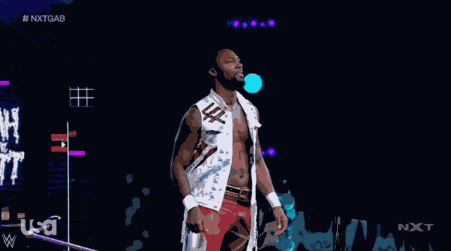 a man in a white vest and red shorts stands on a stage in front of a screen that says nxt gab