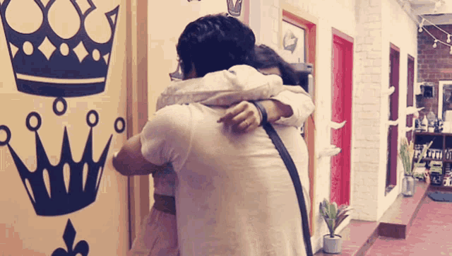 a man and woman hugging in front of a wall with a crown
