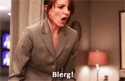 a woman in a suit is standing in a room with her mouth open and says blerg .