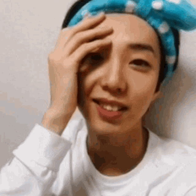 a young man wearing a blue headband is touching his face .