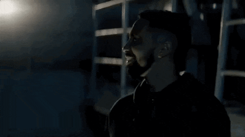 a man in a black hoodie is standing in a dark room looking up .