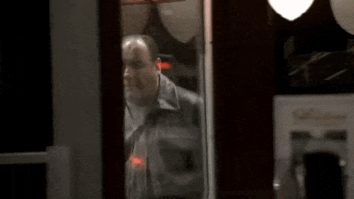 a man in a leather jacket is standing in a doorway in front of a neon sign .