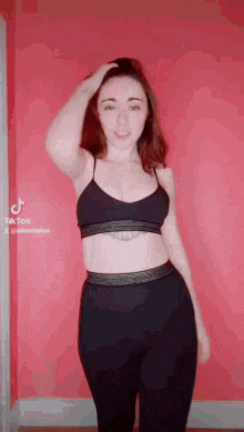 a woman in a crop top and leggings is standing in front of a red wall .